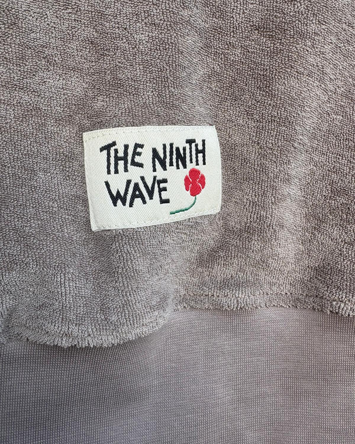 Gray towel with 'The Ninth Wave' label featuring a flower design.