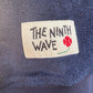Close-up of a Dark Navy Towelling Jumper with 'The Ninth Wave' label featuring a flower design.