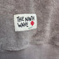 Gray towel with 'The Ninth Wave' label featuring a flower design.